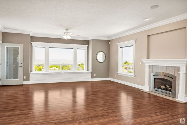 Unfurnished living room featuring heating unit, ceiling fan, wood finished floors, a tiled fireplace, and healthy amount of natural light | Image 13
