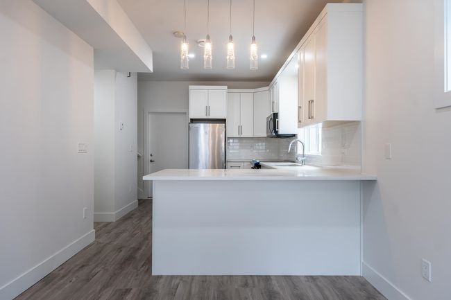 Kitchen with stainless steel appliances, baseboards, decorative backsplash, a peninsula, and dark wood-type flooring | Image 6