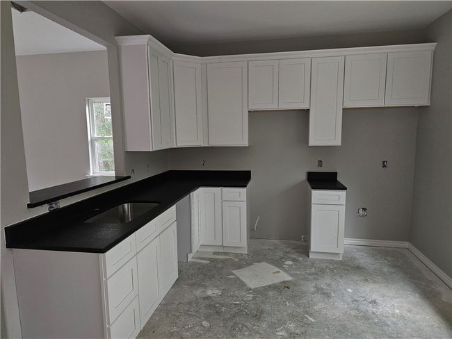 Kitchen featuring white cabinets, a sink, dark countertops, and baseboards | Image 4