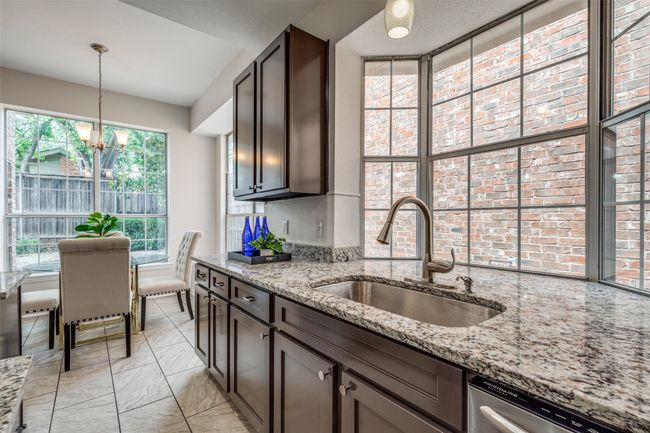 Kitchen with a sink, dishwasher, a chandelier, dark brown cabinets, and light stone counters | Image 12