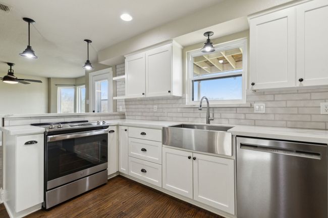 Kitchen featuring dark wood-type flooring, a sink, appliances with stainless steel finishes, a peninsula, and white cabinets | Image 12