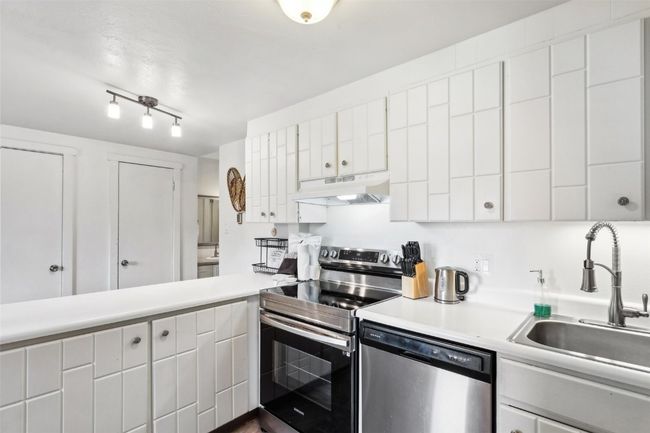 Kitchen with white cabinets, under cabinet range hood, light countertops, a sink, and appliances with stainless steel finishes | Image 14