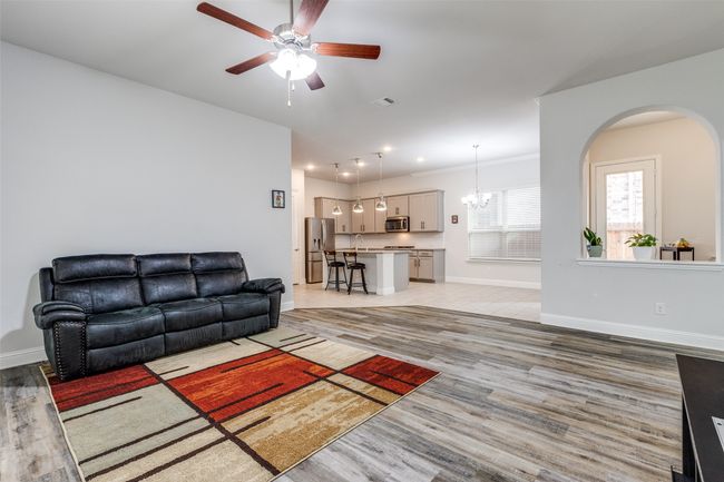 Living area with arched walkways, ceiling fan with notable chandelier, baseboards, and light wood-style floors | Image 8