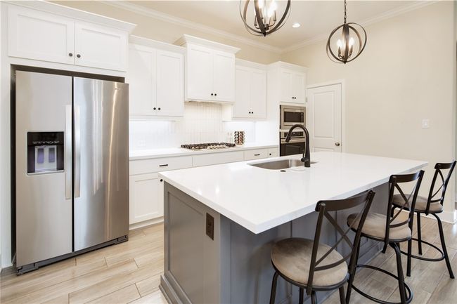 Kitchen featuring appliances with stainless steel finishes, a sink, a center island with sink, white cabinetry, and ornamental molding | Image 8
