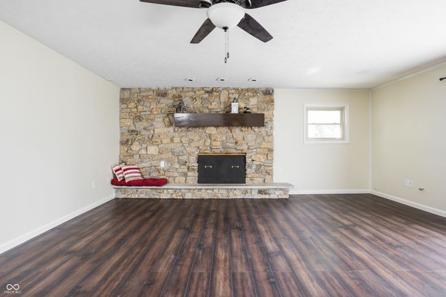 unfurnished living room with wood finished floors, ceiling fan, and a fireplace | Image 9