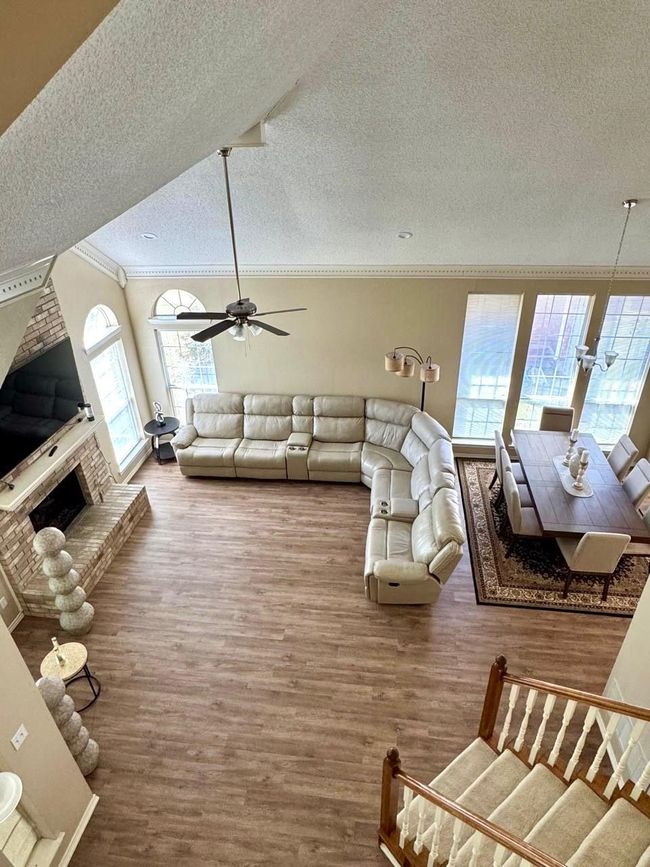 Living room with a textured ceiling, crown molding, a ceiling fan, a brick fireplace, and wood finished floors | Image 18