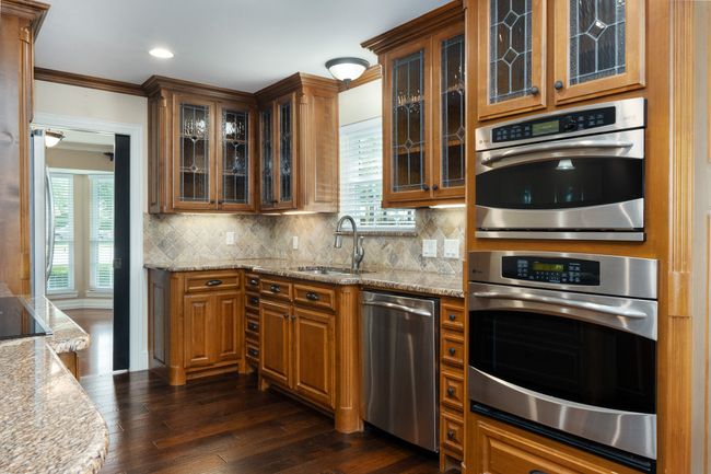 Kitchen with appliances with stainless steel finishes, dark wood-style flooring, brown cabinetry, tasteful backsplash, and ornamental molding | Image 16