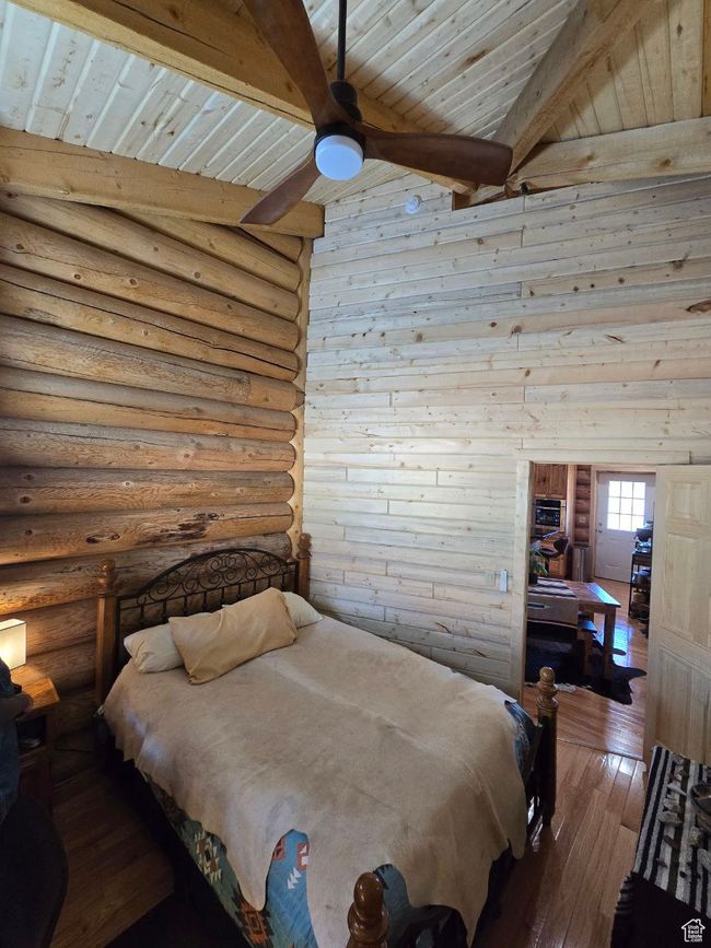 Bedroom with dark wood-type flooring, beam ceiling, wooden ceiling, rustic walls, and a ceiling fan | Image 73