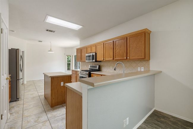 Kitchen with a peninsula, a kitchen island, light countertops, backsplash, and stainless steel appliances | Image 16