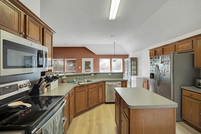 Kitchen featuring stainless steel appliances, light wood-style flooring, a textured ceiling, and brown cabinetry | Image 17