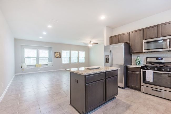 Kitchen with dark brown cabinets, backsplash, a kitchen island, baseboards, and stainless steel appliances | Image 16