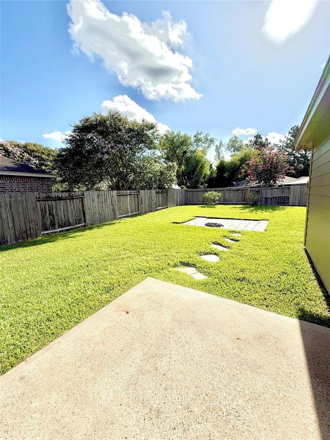 This photo showcases a spacious backyard with a well-maintained lawn, a small patio area, and a wooden fence for privacy. Ideal for outdoor activities and relaxation. | Image 22