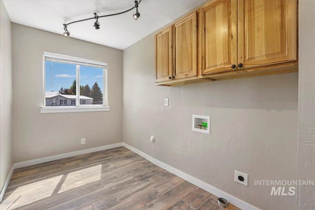 Laundry area featuring hookup for an electric dryer, hookup for a washing machine, cabinet space, wood finished floors, and track lighting | Image 17