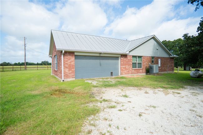 View of side of home featuring brick siding, driveway, a garage, a lawn, and a metal roof | Image 14