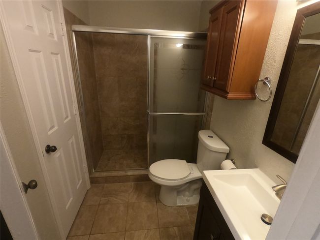 Bathroom with a shower stall, tile patterned flooring, vanity, toilet, and a textured wall | Image 5