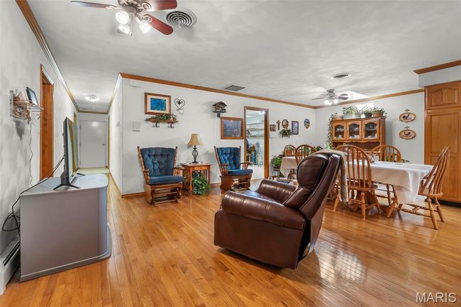 Living room featuring ceiling fan, ornamental molding, light wood-style flooring, and a baseboard heating unit | Image 63