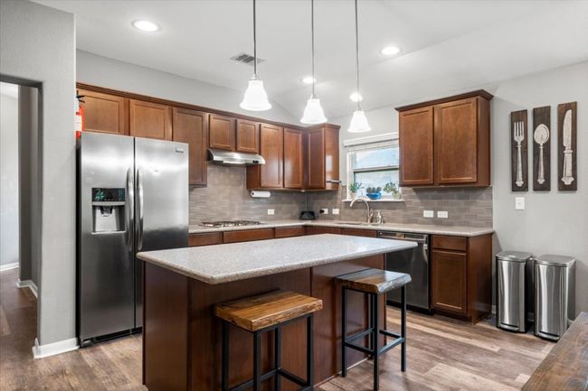 Kitchen with stainless steel appliances, under cabinet range hood, wood laminate floors, a sink, and decorative backsplash | Image 8