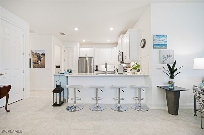 Kitchen with appliances with stainless steel finishes, a peninsula, a kitchen bar, white cabinets, and light countertops | Image 6