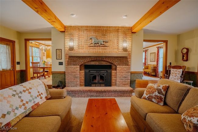 Carpeted family room with beamed ceiling, wainscoting, a chandelier, and a brick fireplace | Image 12