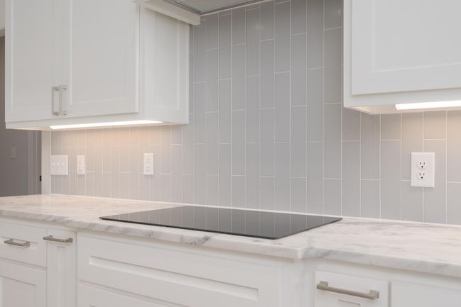 Kitchen featuring light stone countertops, white cabinetry, decorative backsplash, and black electric cooktop | Image 14