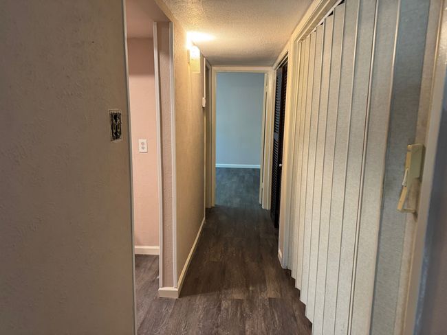 Hall with a textured ceiling, dark wood finished floors, and a textured wall | Image 8
