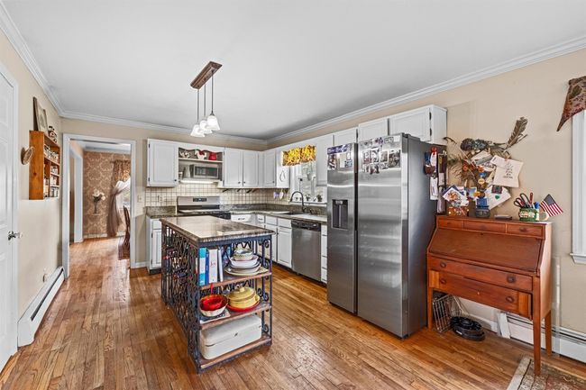 Kitchen with open shelves, a baseboard heating unit, a baseboard radiator, stainless steel appliances, and hardwood / wood-style floors | Image 5