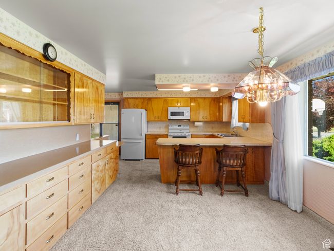 Kitchen featuring white appliances, light colored carpet, a chandelier, and light countertops | Image 10