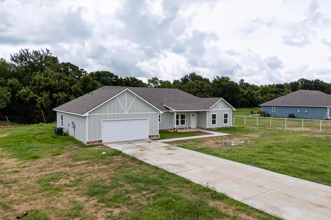 Ranch-style house featuring board and batten siding, concrete driveway, a garage, and a shingled roof | Image 7