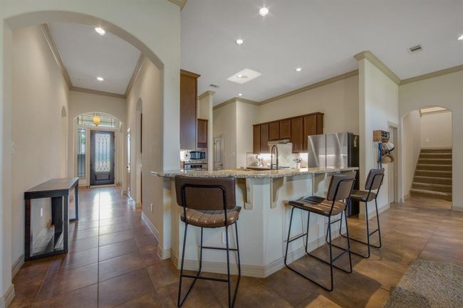 Picture shows the foyer, granite breakfast bar, stairs to media room, arches, crown molding and tile flooring | Image 10