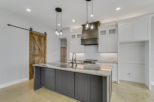 Kitchen with concrete flooring, a sink, backsplash, white cabinets, and baseboards | Image 9