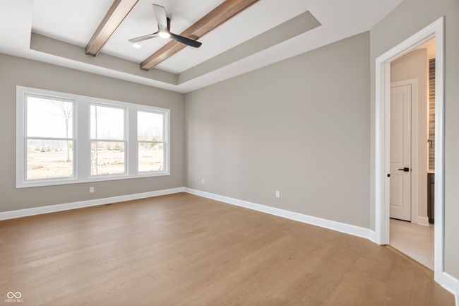 Spacious primary bedroom with ceiling tray and wood beams. large windows offering natural light. | Image 17