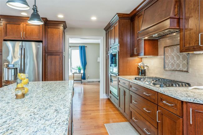 Kitchen featuring appliances with stainless steel finishes, wall chimney exhaust hood, backsplash, light stone counters, and light wood-type flooring | Image 7