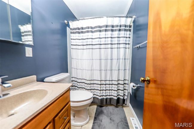 Full bath with toilet, vanity, a shower with shower curtain, and visible vents | Image 4