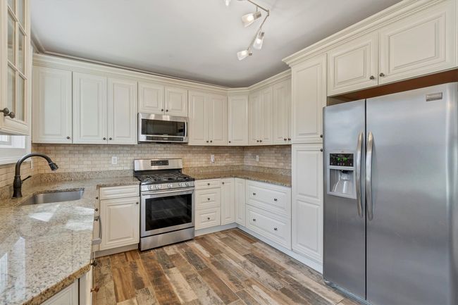 Kitchen featuring appliances with stainless steel finishes, a sink, wood finished floors, and tasteful backsplash | Image 15