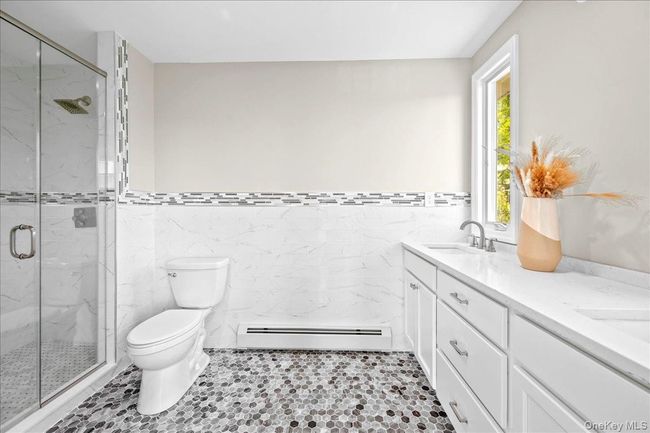 Bathroom featuring baseboard heating, tile walls, toilet, a marble finish shower, and double vanity | Image 28