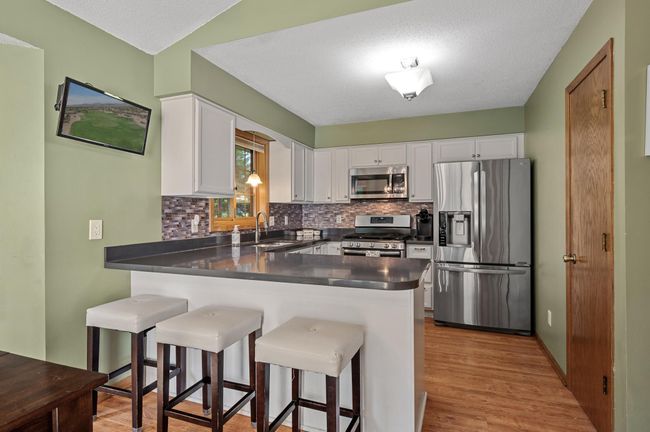 Beautifully updated kitchen features white cabinetry, stainless steel appliances, quartz countertops, and a tile backsplash. | Image 13