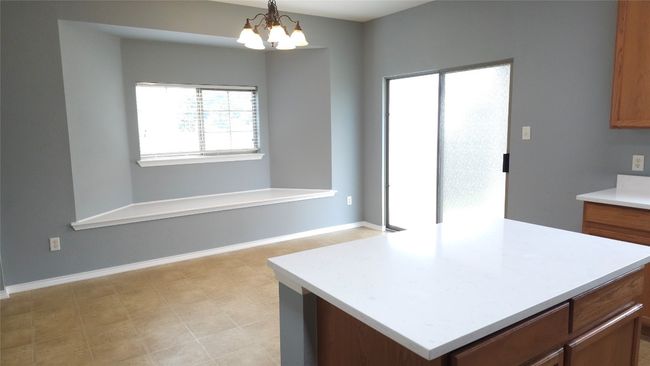 Kitchen featuring light countertops, a chandelier, brown cabinetry, hanging light fixtures, and a kitchen island | Image 5
