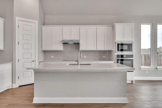 Kitchen featuring white cabinets, a kitchen island with sink, light countertops, under cabinet range hood, and a sink | Image 11