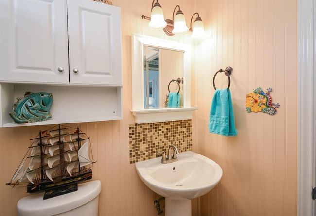 Bath features a pedestal sink with a decorative mosaic backsplash, and a wall-mounted cabinet for storage. Nautical-themed decor, including a model ship and fish ornament, adds character. A bright turquoise towel complements the warm lighting. | Image 26