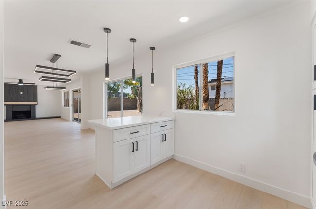 Kitchen with a peninsula, light wood-style flooring, white cabinetry, pendant lighting, and a fireplace | Image 21