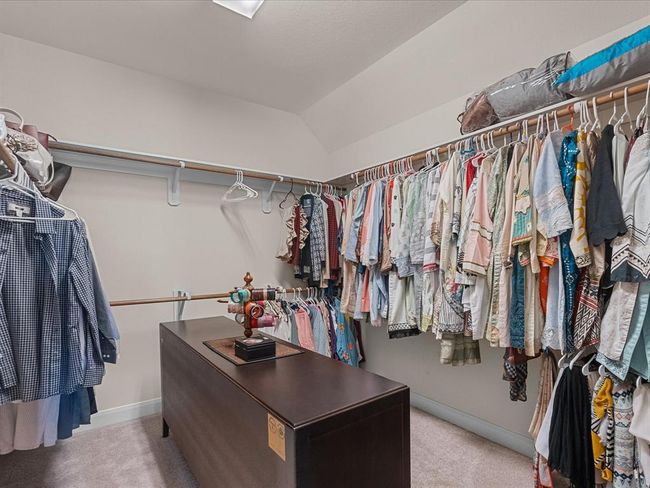 Spacious walk-in closet with ample hanging space and a central island, perfect for organizing clothes and accessories located in primary bedroom. | Image 27