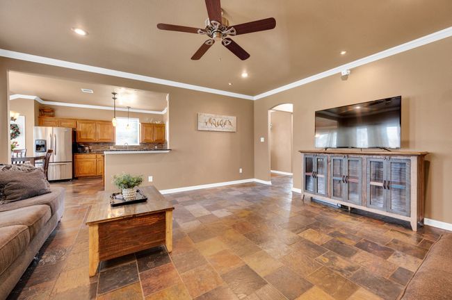 Living area with a ceiling fan, arched walkways, stone tile flooring, crown molding, and recessed lighting | Image 9