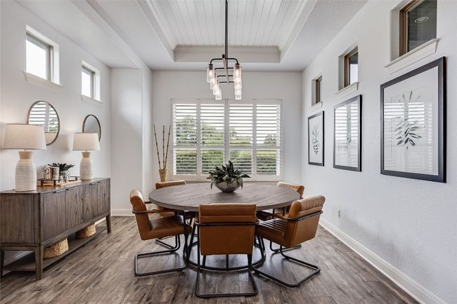 Dining space featuring a raised ceiling, wood finished floors, crown molding, and a chandelier | Image 13
