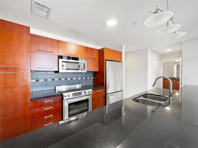Kitchen featuring appliances with stainless steel finishes, a sink, pendant lighting, brown cabinetry, and recessed lighting | Image 9