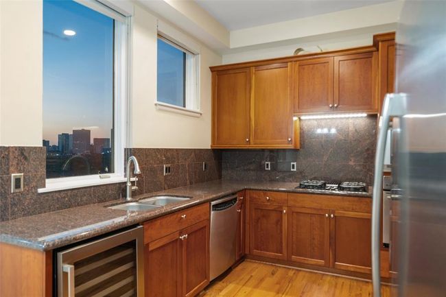 Modern kitchen featuring lots of rich cherrywood cabinetry, sleek granite countertops, gas cooktop and stainless steel appliances, all enhanced by stunning city views. | Image 13