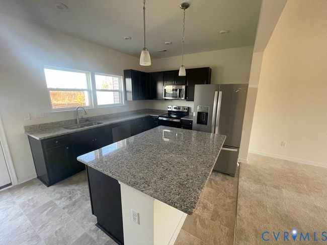Kitchen featuring dark cabinetry, light stone countertops, stainless steel appliances, hanging light fixtures, and a kitchen island | Image 19