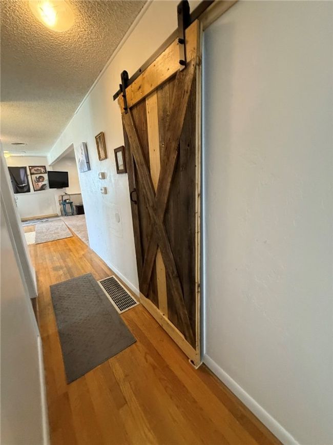 Hallway featuring a barn door, a textured ceiling, wood finished floors, and baseboards | Image 9