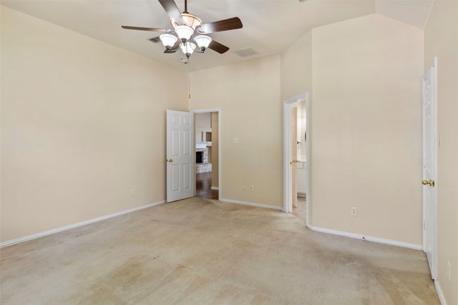 Unfurnished bedroom with light colored carpet, baseboards, high vaulted ceiling, ensuite bath, and ceiling fan | Image 13