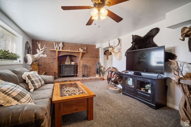 Living area featuring brick wall, a ceiling fan, carpet flooring, and a wood stove | Image 14
