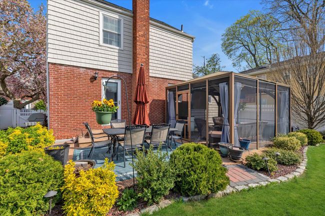 Rear view of house with brick siding, a sunroom, a chimney, and a patio | Image 15